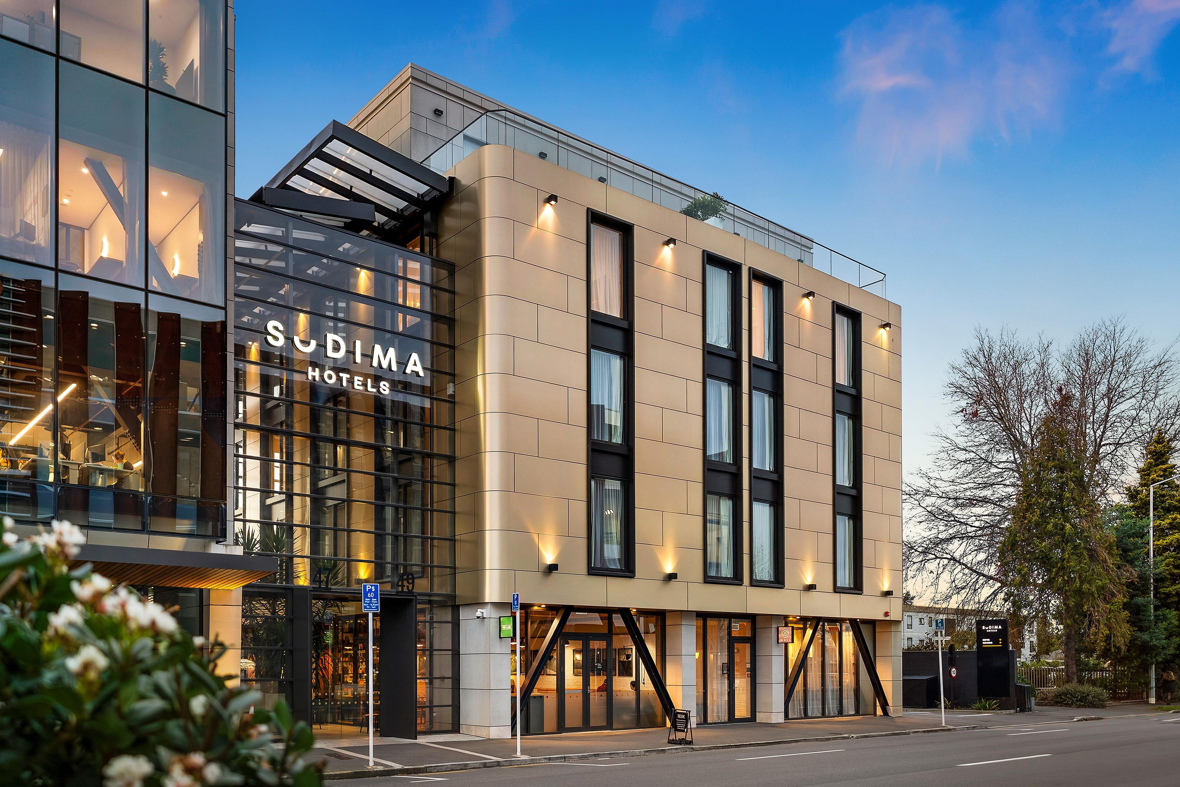 A modern hotel building with a glass facade, signage for 'Sudima Hotels', and a visible entrance.