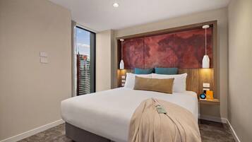 Habitación de hotel con una cama grande, vista a un paisaje urbano por la ventana y un cabecero moderno.