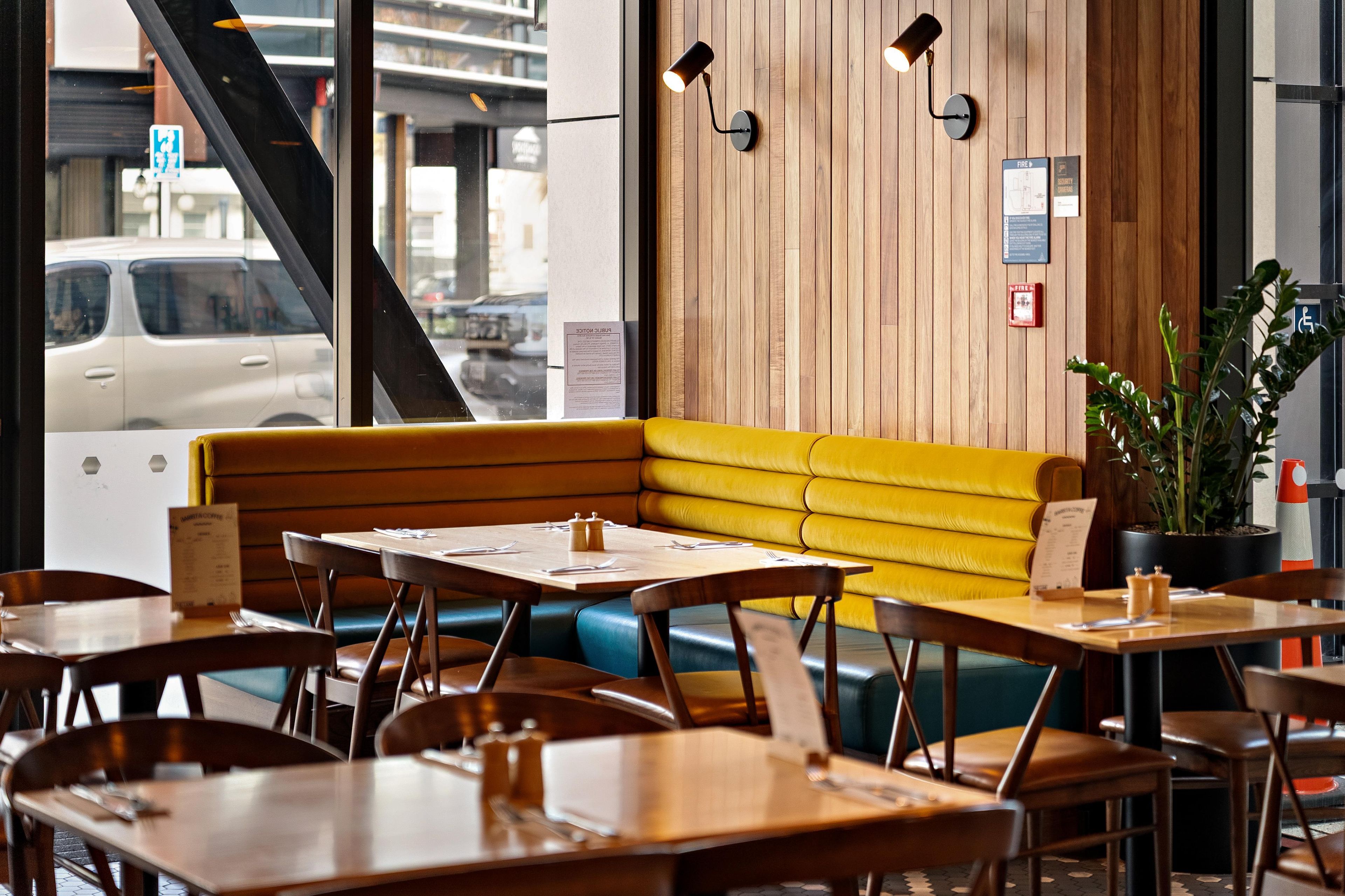 A restaurant interior with a wooden wall, yellow seating, and tables with menus.