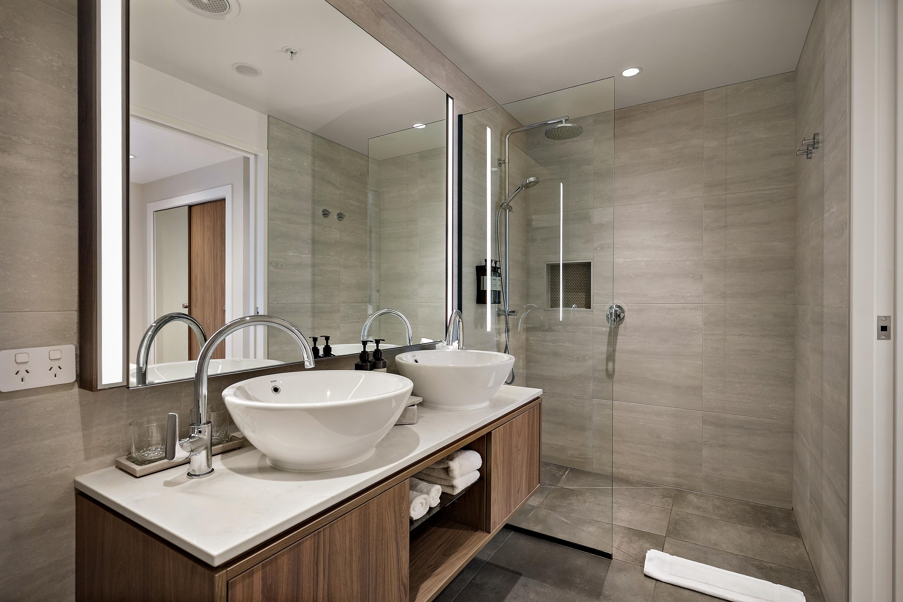 A modern bathroom with two sinks, a shower, and a large mirror.