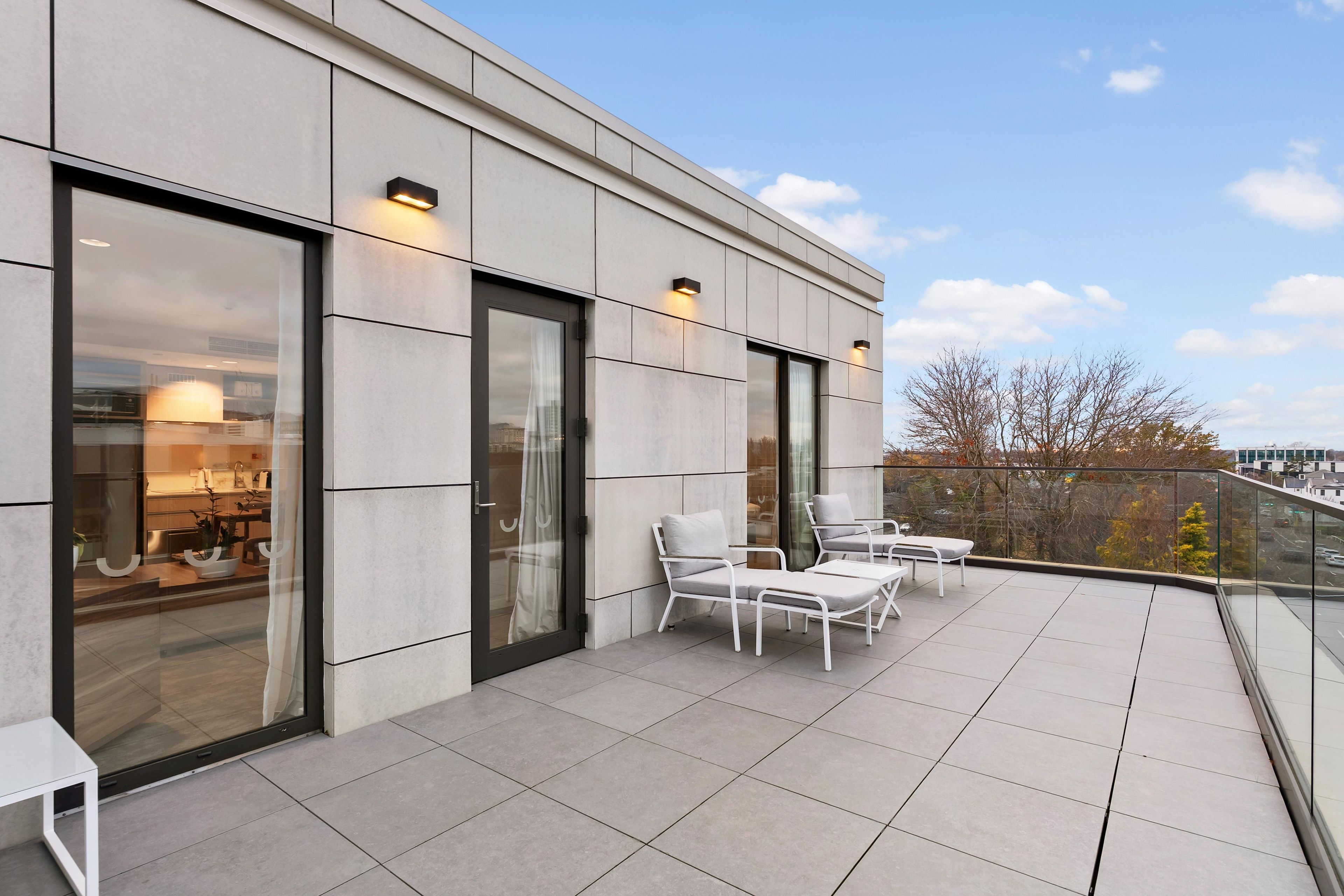 A modern building with a balcony featuring outdoor seating and large windows.