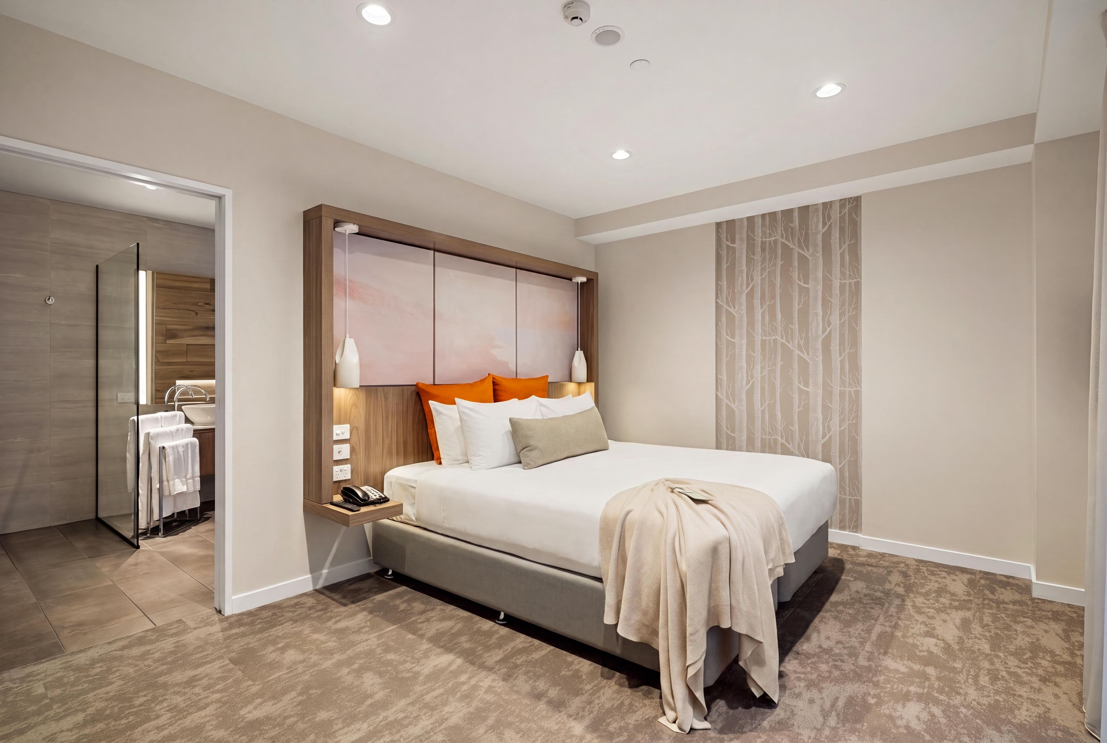 A modern bedroom with a large bed, bedside lamps, a nightstand, and a mirror.