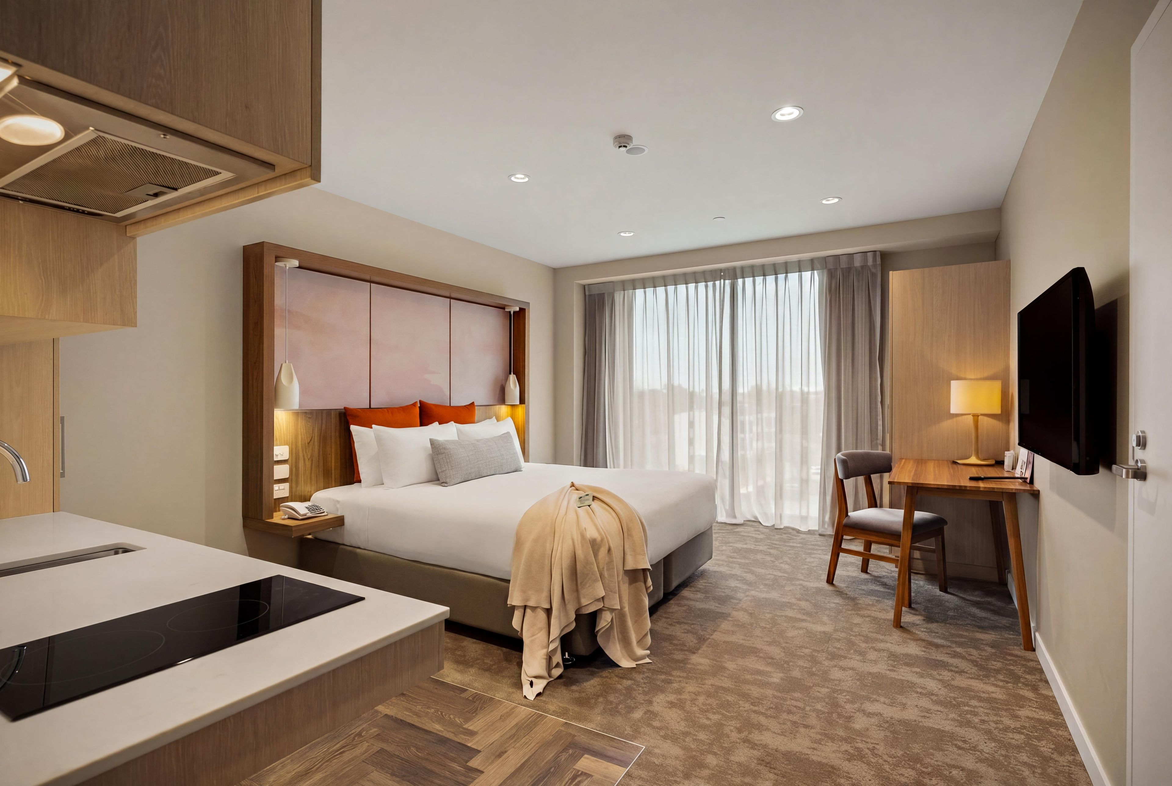 A hotel room with a bed, a desk, a chair, a TV, a phone, and a bathroom with a bathtub and sink.