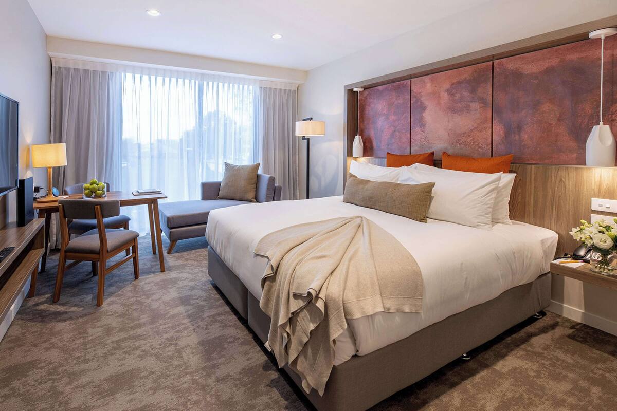 A hotel room with a large bed, a desk with a chair, a TV, and a lamp.