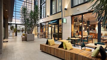 An indoor seating area with a modern design, featuring a long wooden bench with cushions and a glass partition separating the seating area from the dining space.