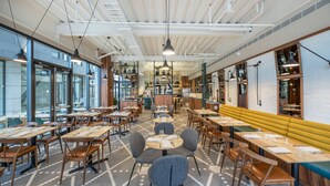 A modern restaurant interior with high ceilings, pendant lighting, and a mix of wooden and upholstered furniture.