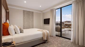 A hotel room with a bed, a desk with a telephone, a flat-screen TV, and a sliding glass door leading to a balcony.