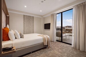 Une chambre d’hôtel équipée d’un lit, d’un bureau avec un téléphone, d’un téléviseur à écran plat et d’une porte-fenêtre coulissante donnant sur un balcon.