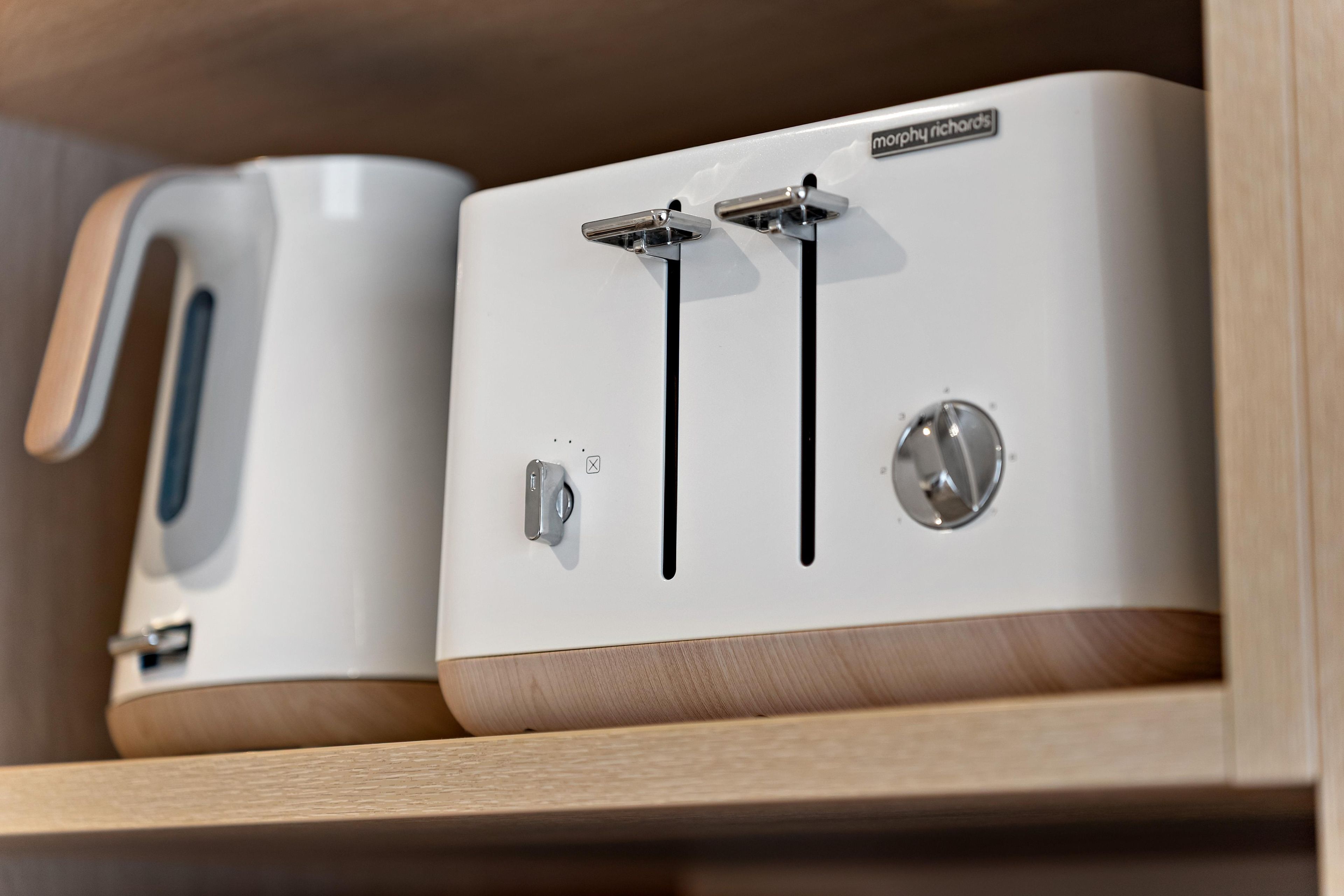 Two white appliances with a handle and a control panel, likely a toaster and a kettle, on a wooden shelf.