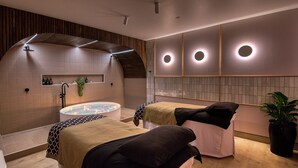A modern spa room with a central hot tub, two massage beds, and a wooden ceiling design. - Sudima Christchurch City (Christchurch)
