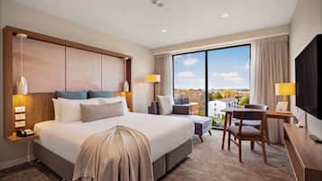 A hotel room with a large bed, bedside lamps, a desk with a chair, a television, and a view of the city.