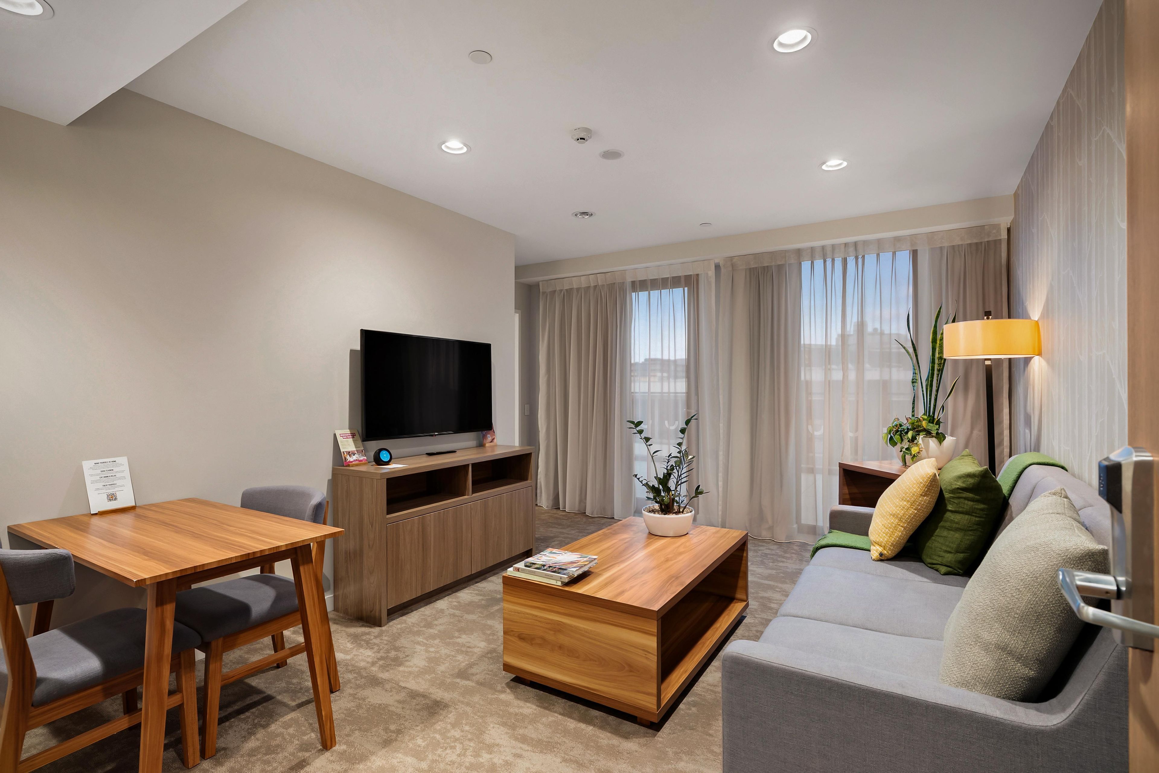 Une chambre d’hôtel moderne équipée d’un téléviseur à écran plat, de meubles en bois, d’un canapé, d’une table basse et d’une plante en pot.