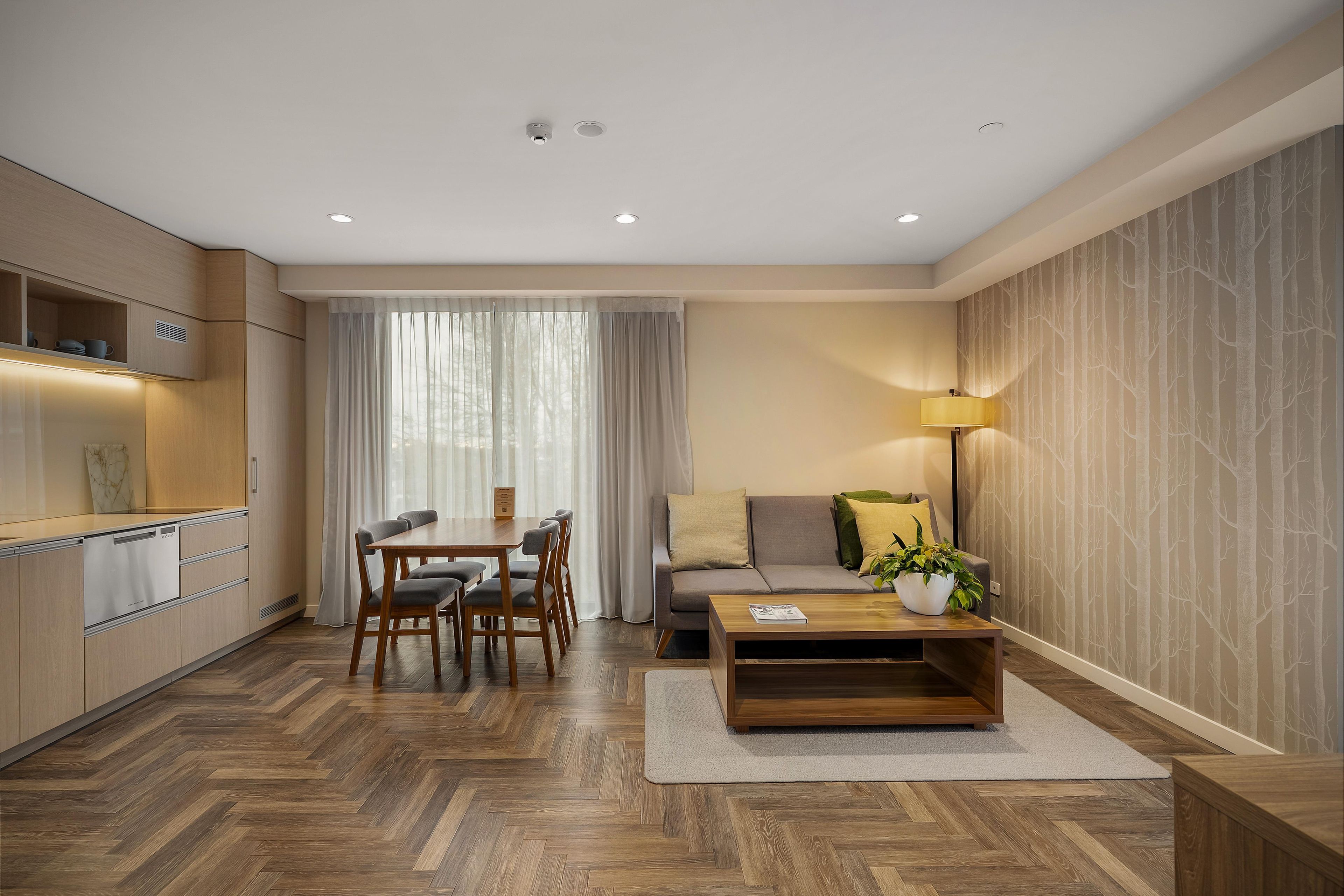 A modern living space with a dining area, sofa, coffee table, and a kitchen with built-in appliances.