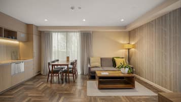 A modern living space with a dining area, sofa, coffee table, and a kitchen with built-in appliances.
