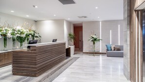 A modern reception area with a wooden reception desk, potted plants, and a grey sofa.