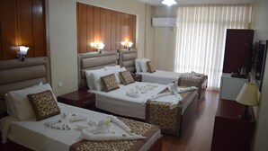 Une chambre d’hôtel avec quatre lits, chacun équipé de serviettes et d’oreillers, avec des têtes de lit en bois et un téléviseur à écran plat.