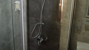 Une cabine de douche moderne dotée d’une porte en verre, d’un pommeau de douche à main et d’un robinet mural.