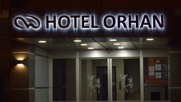 L’entrée d’un hôtel, avec une enseigne lumineuse indiquant « HÔTEL ORHAN » et des panneaux de verre décoratifs.