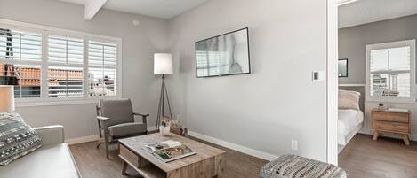 Un salon moderne avec un canapé, un fauteuil et une table basse, une lampe et une œuvre d’art encadrée accrochée au mur.
