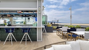 A rooftop bar with a view of the beach, featuring bar stools, tables, and a variety of bottles. - Sea Sprite Beach Club (Hermosa Beach)