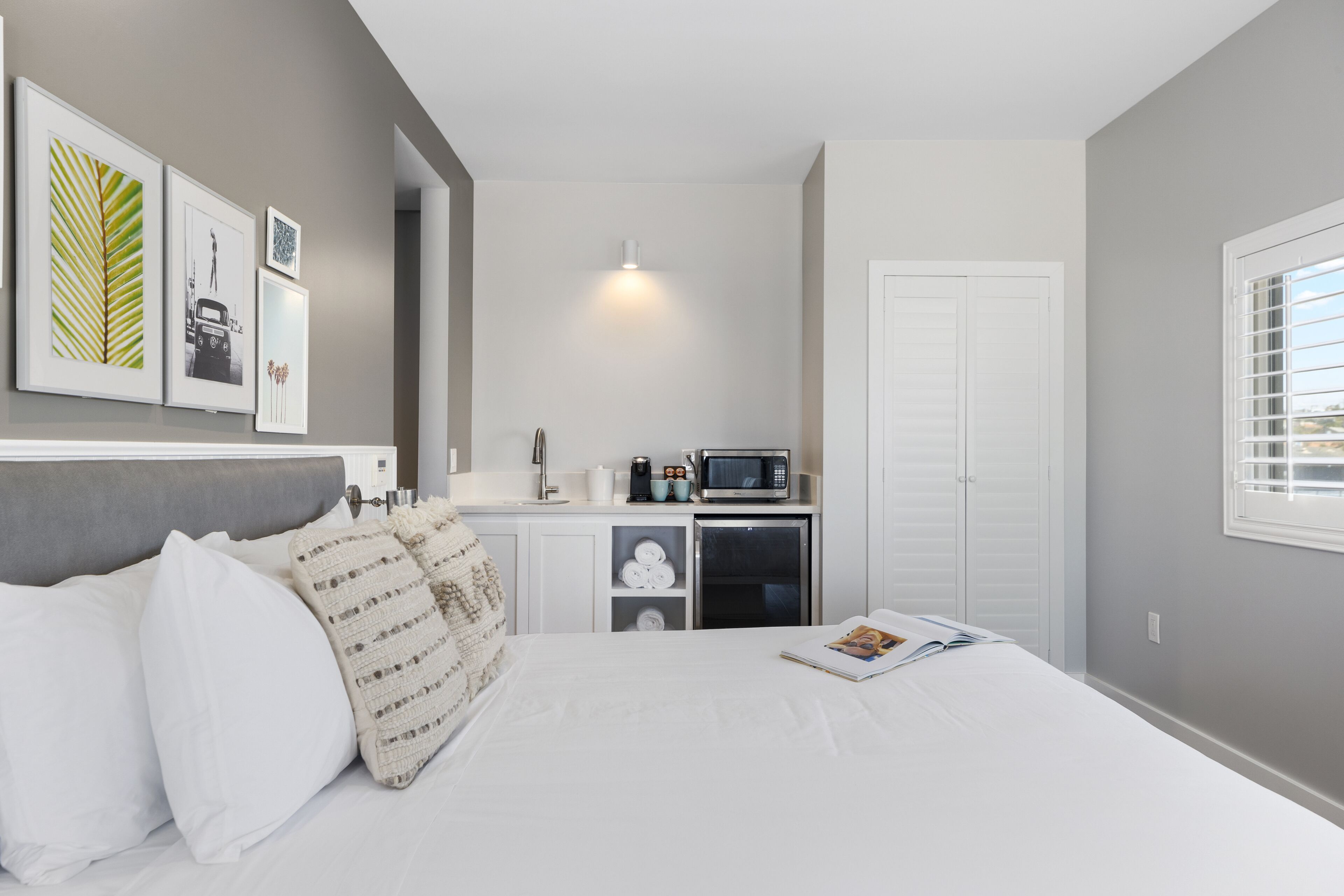 Quarto com cama, travesseiros, mesa de cabeceira, micro-ondas, frigorífico e porta.