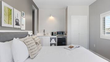 Quarto com cama, travesseiros, mesa de cabeceira, micro-ondas, frigorífico e porta.