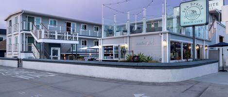 A beachfront building with a 'Surfer Girl' sign, a balcony, and a beach club sign.