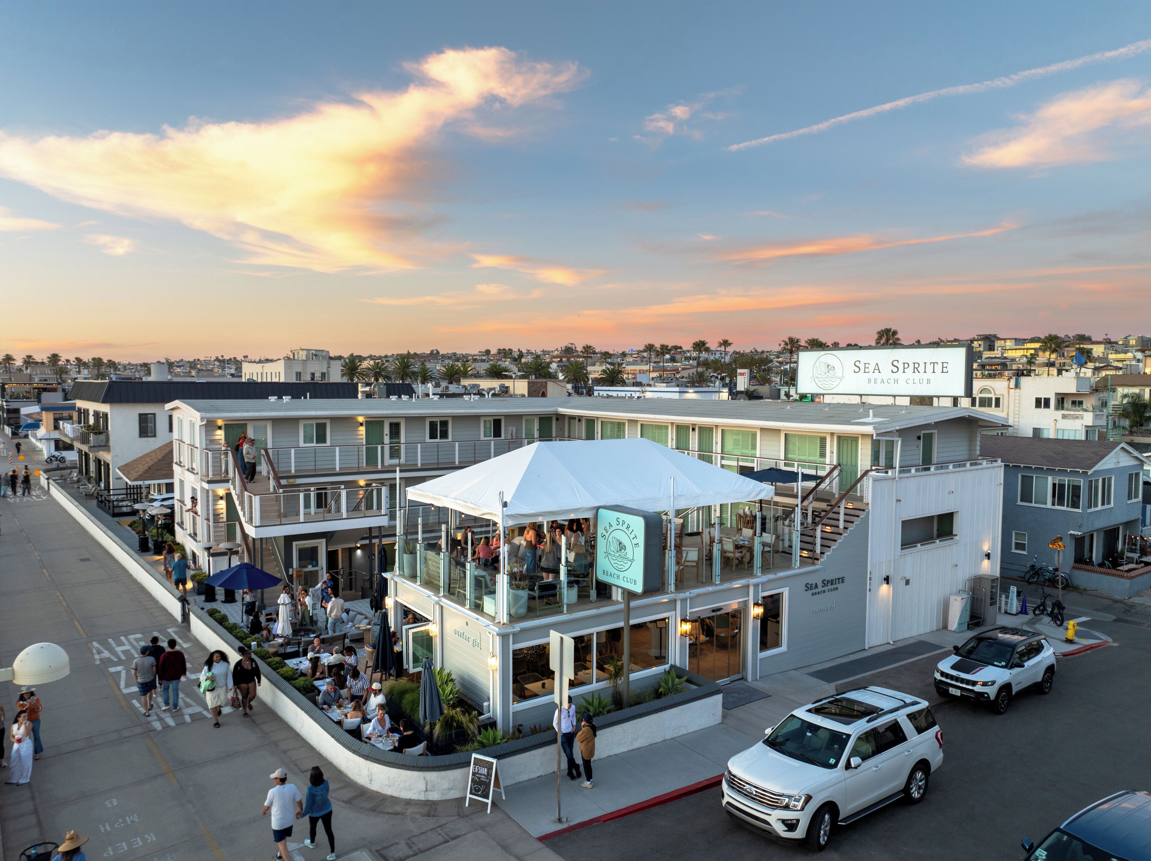 Ein Küstengebäude mit der Aufschrift 'SEA SPITE BEACH CLUB', Au ßenbereich mit Sitzgelegenheiten und einem weißen Zelt.