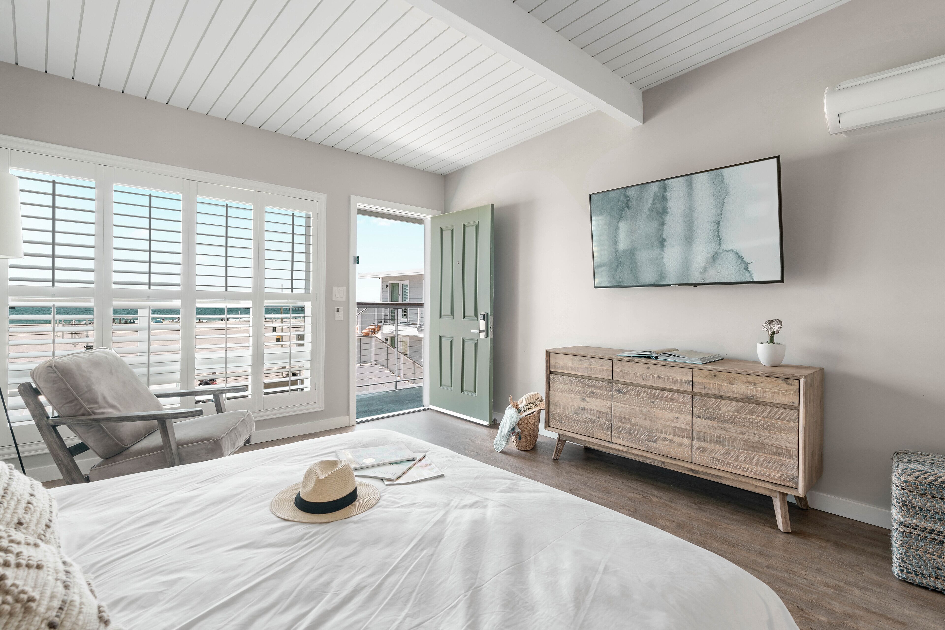 A bedroom with a large bed, a wooden dresser, a chair, and a view of the outside.