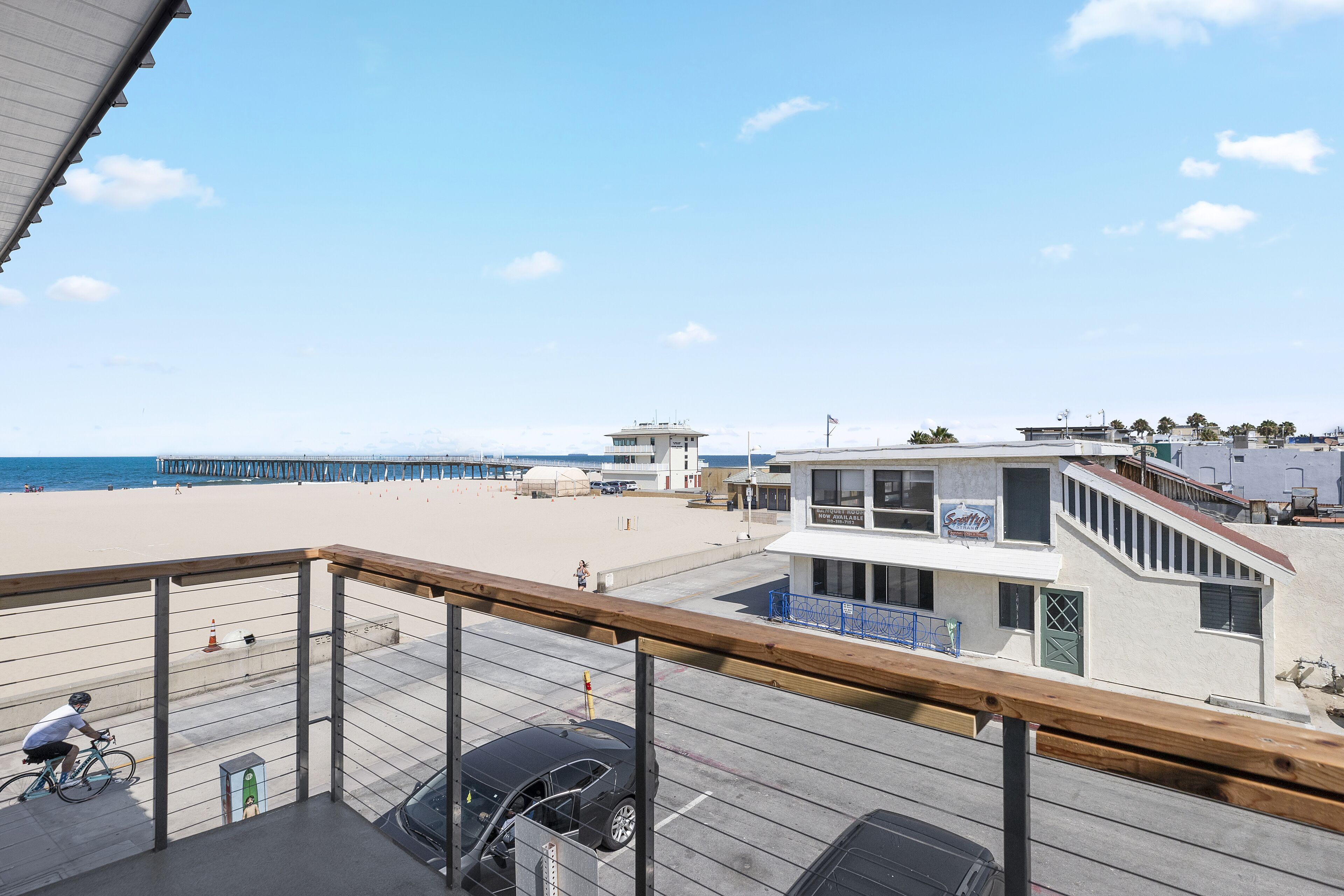 Vista desde un balcón sobre una playa arenosa, un estacionamiento y un edificio con un letrero que dice 'Sandy Beach'.