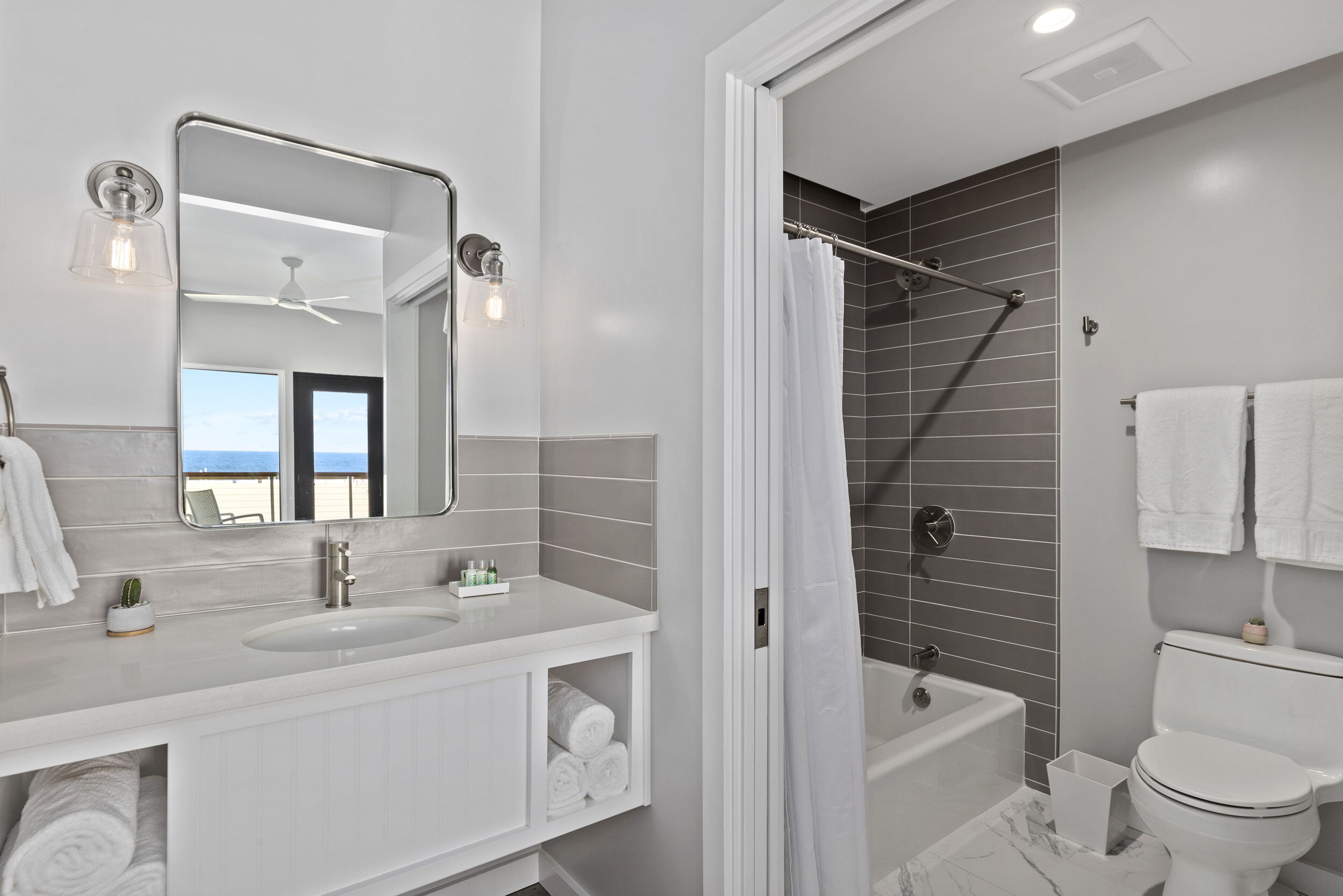 A modern bathroom with a large mirror, two sinks, a shower, and a toilet.
