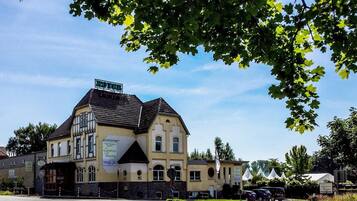 Ein zweistöckiges Gebäude mit einem Schild, das es als Hotel kennzeichnet. Das Gebäude hat einen traditionellen Baustil mit einem Satteldach und einem Balkon im zweiten Obergeschoss.