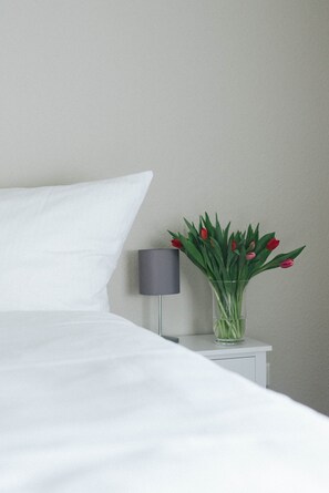 A neatly made bed with white bedding, a small bedside table with a lamp, and a vase with red tulips. - Landhaus Begatal (Doerentrup)