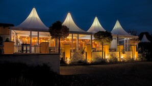 A restaurant with a glass facade and multiple conical roofs, illuminated by warm lighting. - Landhaus Begatal (Doerentrup)