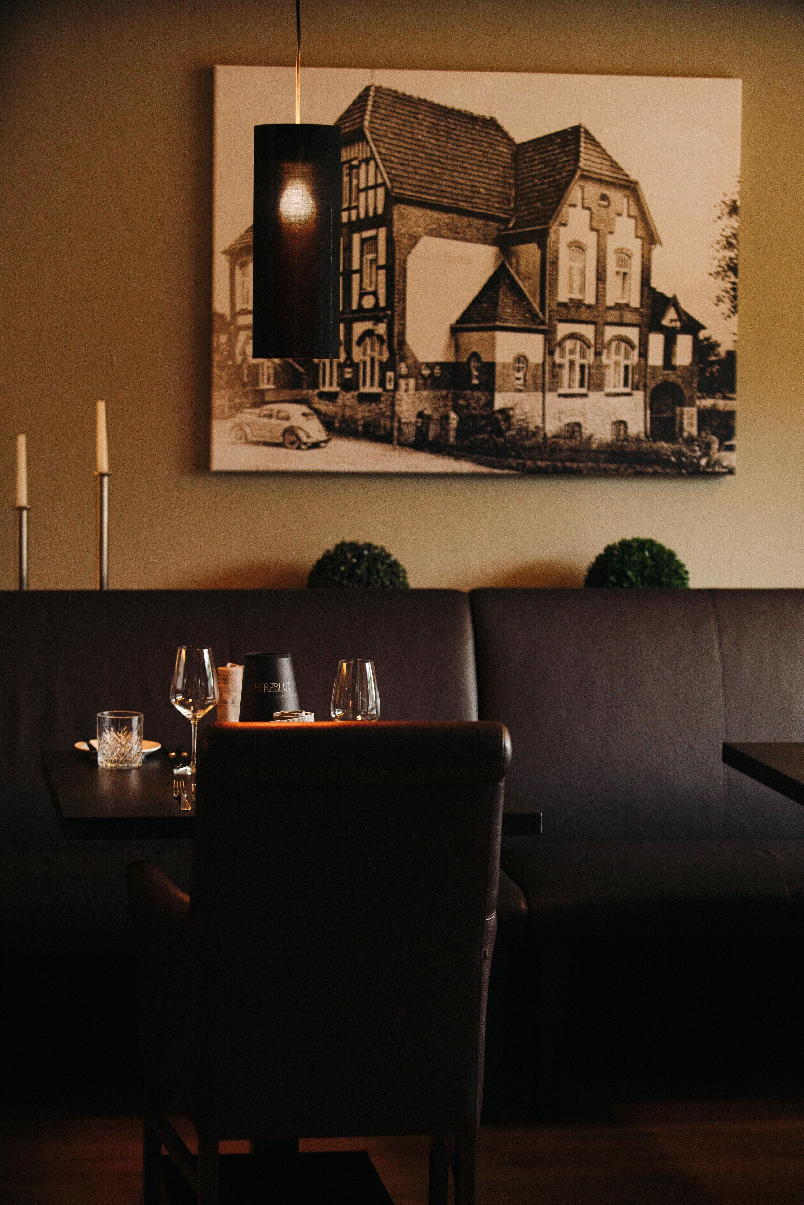 A dining area with a table set for two, a framed black and white photograph on the wall, and a dark brown leather sofa.