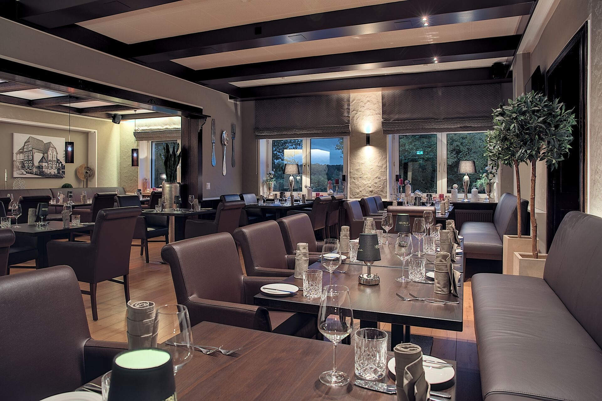 Un restaurant moderne avec des tables en bois foncé, des sièges en cuir et de grandes fenêtres donnant sur l’extérieur.