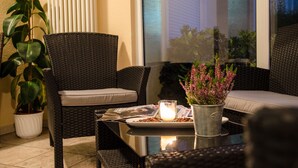 A cozy outdoor seating area with wicker furniture, a table with a candle, and potted plants. - Landhaus Begatal (Doerentrup)