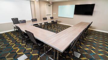 A conference room with a long table, chairs, a projector screen, and a TV.