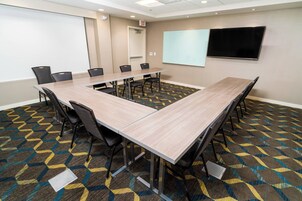 A conference room with a long table, chairs, a projector screen, and a TV.