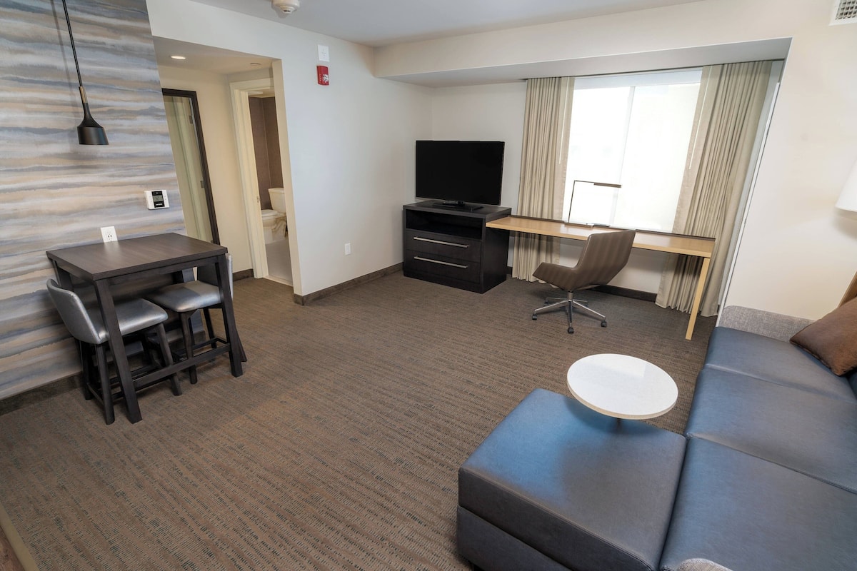 Une chambre d’hôtel moderne équipée d’une télévision à écran plat, d’un bureau avec une chaise, d’un canapé et d’une petite table ronde.