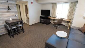 A modern hotel room with a flat-screen TV, a desk with a chair, a sofa, and a small round table.
