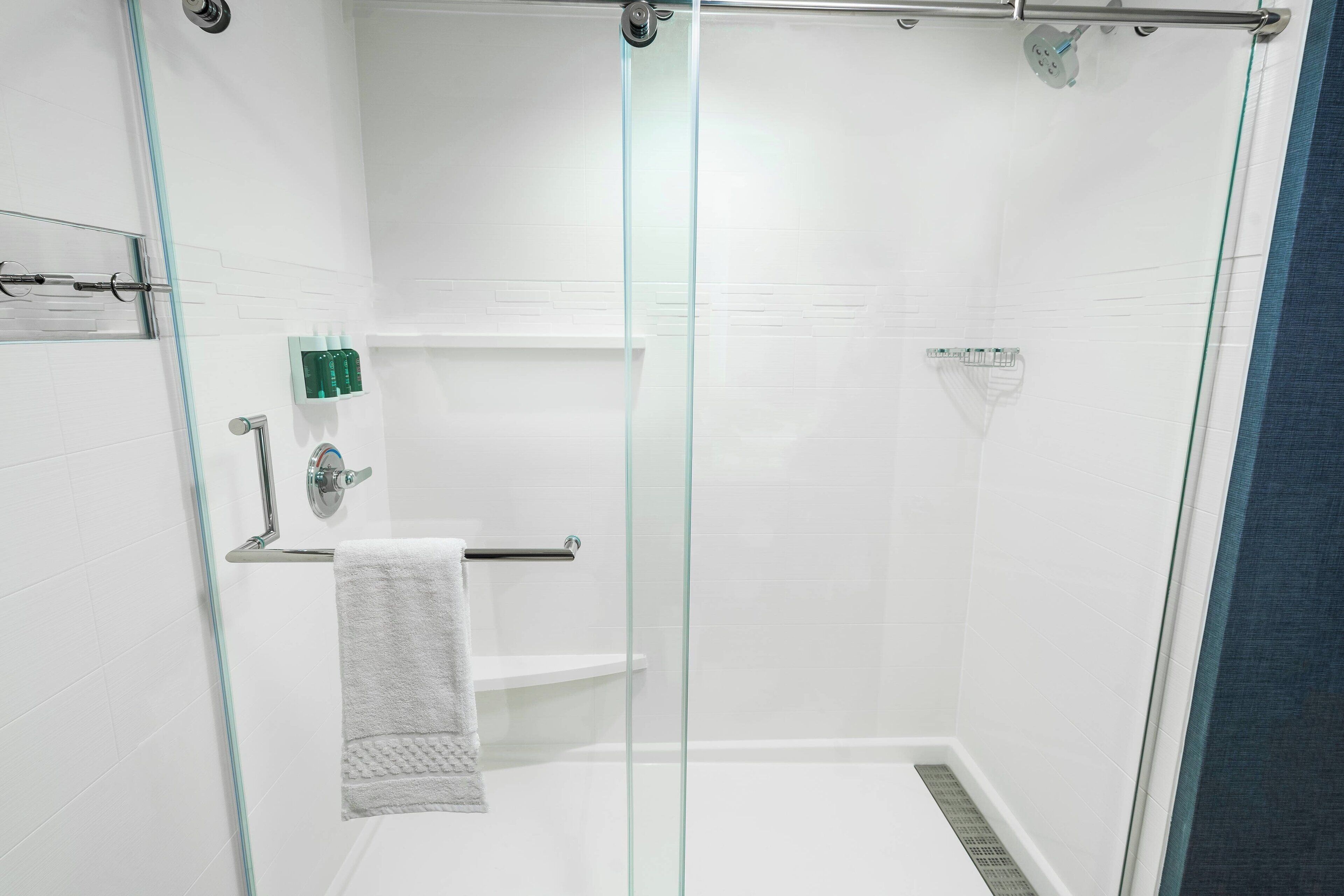 A modern shower area with glass doors, a towel rack, and a shelf with toiletries.