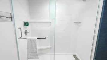 A modern shower area with glass doors, a towel rack, and a shelf with toiletries.