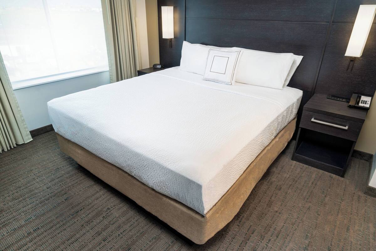 Une chambre d’hôtel avec un grand lit, une table de chevet avec un téléphone et une lampe fixée au mur.