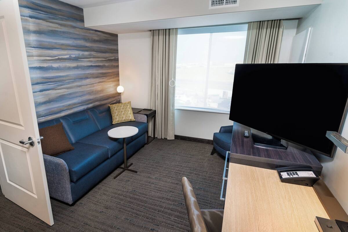 Une chambre d’hôtel avec un canapé bleu, une petite table ronde, un téléviseur et un bureau avec une balance.