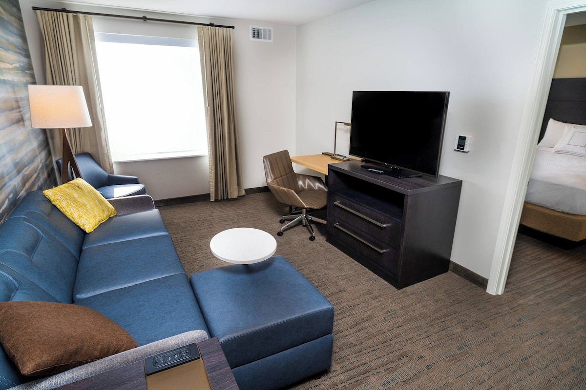 Une chambre d’hôtel avec un canapé bleu, une petite table ronde, une télévision et un lit.
