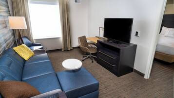 Ein Hotelzimmer mit einem blauen Sofa, einem kleinen runden Tisch, einem Fernseher und einem Bett.