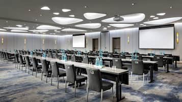 A conference room with long tables, chairs, and a large screen.