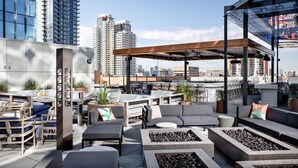 A rooftop lounge with outdoor seating, fire pits, and a view of the city skyline.