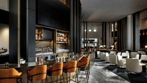 A modern bar area with a long counter, multiple bar stools, and a variety of bottles and glasses.
